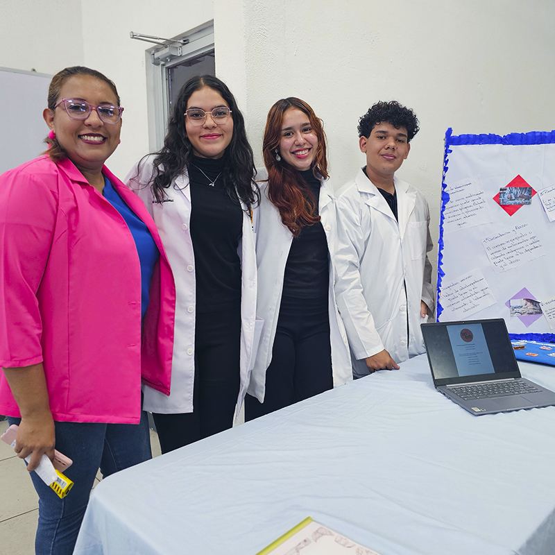 Estudiantes con gabacha presentando un proyecto